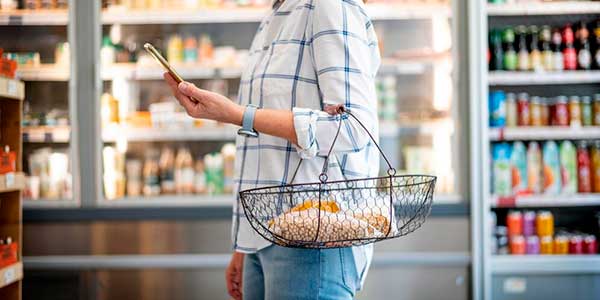 Mujer consultando el móvil en el supermercado. Barómetro consumo